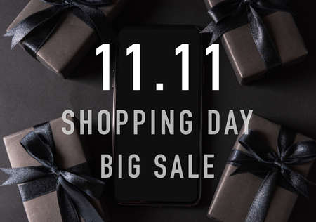 11:11 sale shopping concept, Top view of gift box wrapped black paper and black bow ribbon present around a smartphone with 11.11 shopping and big sale text, studio shot on dark backgroundの写真素材