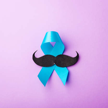 Black mustache paper and light blue ribbon, studio shot isolated on purple background, Prostate...