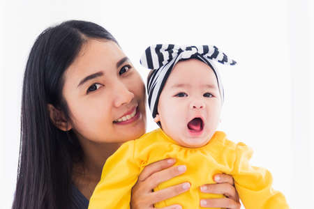 Portrait of beautiful young Asian mother playing and smiling together with his newborn little baby at home, Parent mom and little kid relaxing in the bedroom, Family having fun togetherの写真素材