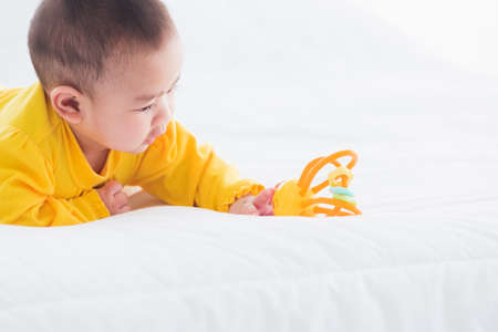Portrait of beautiful young Asian newborn little baby prone on the bed at home, Happy baby smile wears a yellow shirt relaxing in the room, Family morning at homeの写真素材