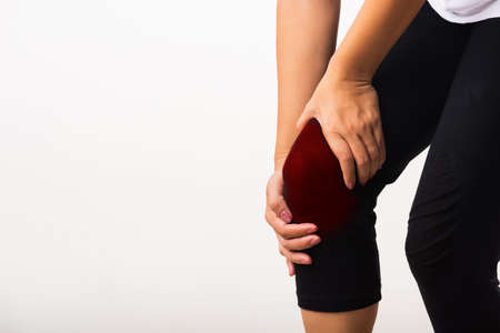 Closeup young woman aches to suffer from pain knee and she uses hand joint hold knee agony, studio shot isolated on white background Rheumatism healthcare and medical physiotherapy therapy conceptの写真素材