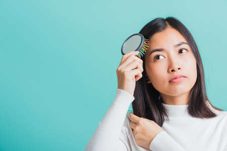 Young beautiful Asian woman upset with a comb and problem hair, Portrait female shocked suffering from hair loss problem, studio shot isolated on a blue background, medicine health conceptの写真素材