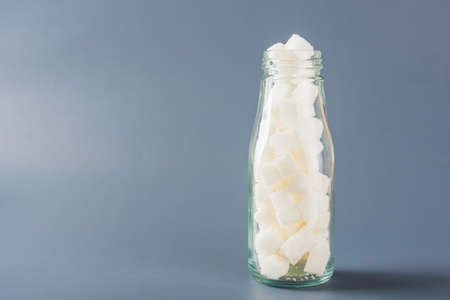 Glass bottle full of white sugar cube sweet food ingredient, studio shot isolated on gray background, health high blood risk of diabetes and calorie intake concept and unhealthy drinkの写真素材