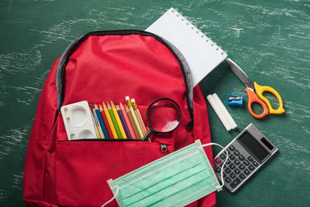 Top view of stylish red school bag backpack at a green chalkboard with face mask protection and stationery, Back to school education new normal during outbreak COVID-19 or coronavirus conceptの写真素材