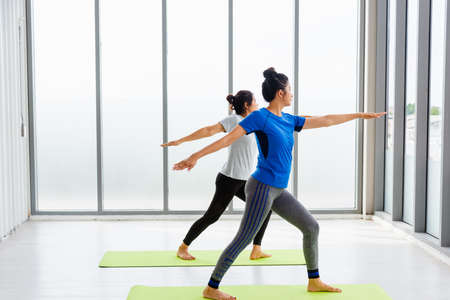 Two Asian women sporty attractive people practicing yoga lesson together, working out at the fitness...