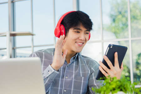 Asian young business man happiness with red headphones he sitting on desk workplace using digital...
