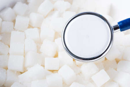 Sugar cube sweet food ingredient texture background and doctor stethoscope, studio shot health high...