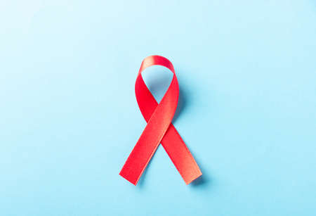 Red bow ribbon symbol HIV, AIDS cancer awareness with shadows, studio shot isolated on blue background, Healthcare medicine concept, World AIDS Dayの写真素材