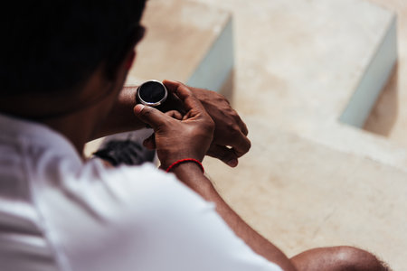 Close up Asian young athlete sport runner black man wear modern time smart watch he sitting resting before training running at the outdoor street health park, healthy exercise before workout conceptの写真素材