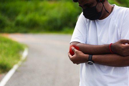 Close up Asian young sport runner black man wear watch he having elbow pain and use hands joint hold elbow while exercising at the outdoor street health park, healthy exercise Injury from workoutの写真素材
