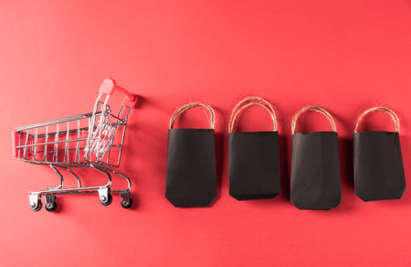 Black Friday sale shopping concept, Black shopping bags and shopping cart, studio shot isolated on red backgroundの写真素材