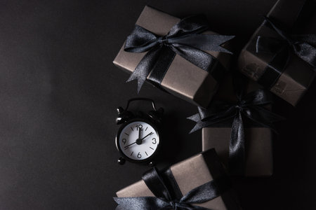 Black Friday sale shopping concept, Top view of gift box wrapped in black paper and black bow ribbon and black alarm clock, studio shot on black backgroundの写真素材