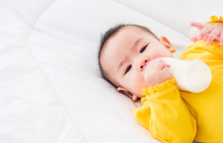 Asian beautiful little baby girl wearing a yellow dress eat milk sleeping feeding lying on the white...