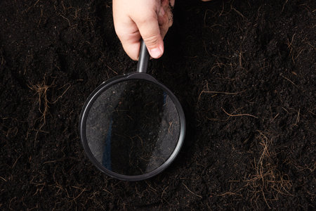 Top view of child hand hold magnifying glass for check black soil at the garden, Concept of global pollution, Save Earth and World Soil Dayの写真素材
