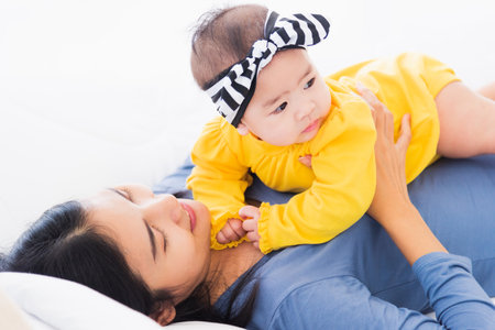 Portrait of beautiful young Asian mother playing and smiling together with his newborn little baby...