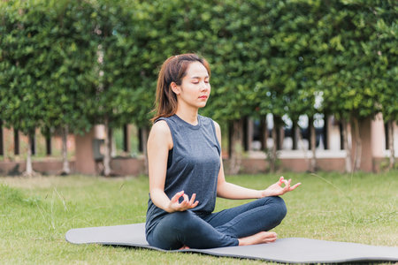 Asian young woman doing yoga outdoors in meditate lotus pose sitting on green grass with closed eyes at the garden park, health care conceptの写真素材