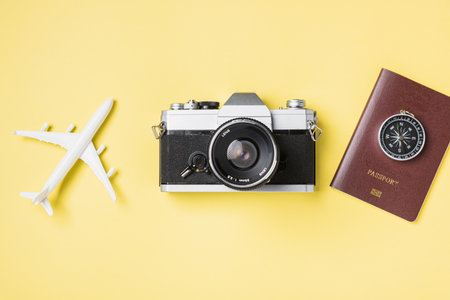 Flat lay top view mockup retro camera films, airplane, traveler tropical accessories on a yellow background with copy space, Vacation summer travel and business trip conceptの写真素材