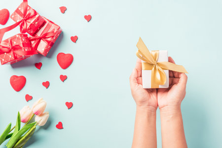 Valentine's day and birthday. Woman hands holding gift or present box decorated and red heart surprise on blue background, Female's hand hold gift box package in craft paper Top view flat layの写真素材