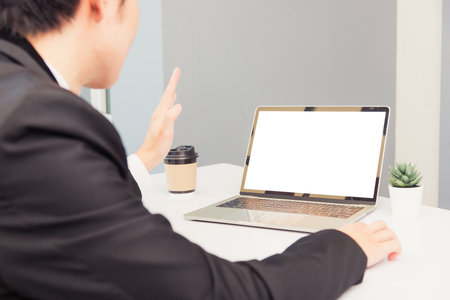 Work from home, Asian young businessman smile wearing suit video conference call or facetime by laptop computer raise your hand to say hello on desk at home officeの写真素材
