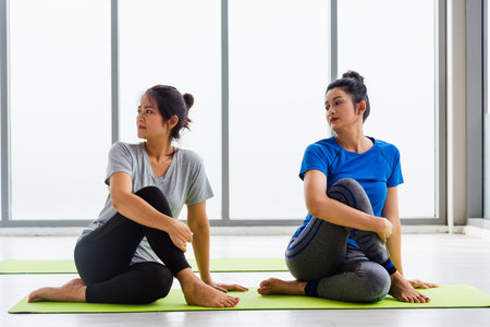 Two Asian women sporty attractive people practicing yoga lesson together, working out at the fitness GYM, Young and senior female exercising do yoga in yoga classes, sport healthy lifestyleの写真素材