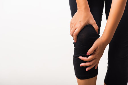Closeup young woman aches to suffer from pain knee and she uses hand joint hold knee agony, studio shot isolated on white background Rheumatism healthcare and medical physiotherapy therapy conceptの写真素材
