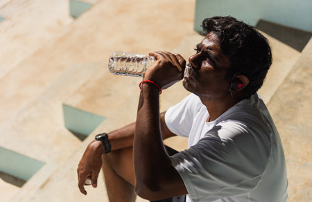 Close up Asian young sport runner black man wear athlete headphones he drinking water from a bottle after running at the outdoor street health park, healthy exercise workout conceptの写真素材