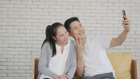 Happy Asian beautiful family couple husband and wife laughing sitting on sofa in the living room...