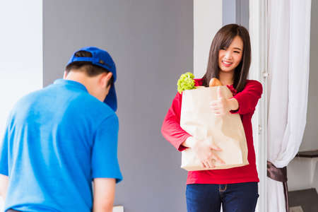 Asian young delivery man in blue uniform making grocery service giving fresh vegetables and fruits...