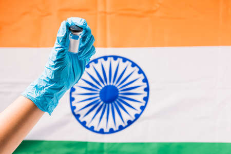 Hands of doctor wear gloves holding coronavirus (COVID-19) vial vaccine and syringe on flag India...