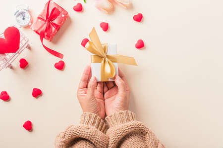 Valentine's day and birthday. Woman hands holding gift or present box decorated and red heart surprise on cream pastel background, Female's hand hold gift box package in craft paper Top view flat layの写真素材