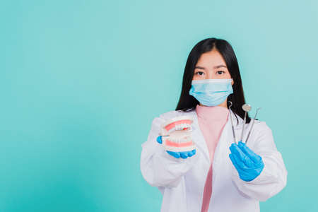 Asian beautiful woman dentist holding professional tool and model teeth denture, female doctor checking denture studio shot isolated on blue background. Dental hygiene surgery health care conceptの写真素材