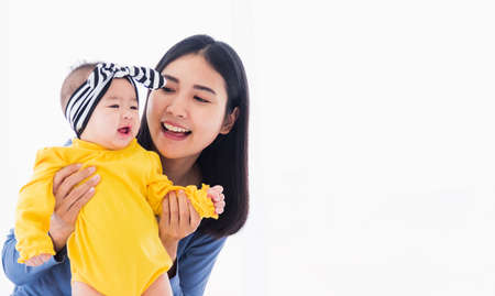 Portrait of beautiful young Asian mother playing and smiling together with his newborn little baby at home, Parent mom and little kid relaxing in the bedroom, Family having fun togetherの写真素材