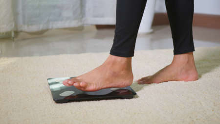 Asian young woman leg stepping standing on floor electric scales, female working out at home in living room, female stand on digital weighing machine. Healthy weight loss control concept, slow motionの写真素材