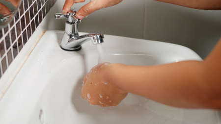 Closeup young woman hands using soap and washing hands under the water tap, female wash their palms with white bubbles in the sink at hotel bathroom to hygiene protect her from Covid-19の写真素材