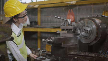 Asian professional mechanical engineer or operation woman wearing uniform goggles safety working on workshop metal lathe industrial manufacturing factory, Heavy industry lathe worker womanの写真素材