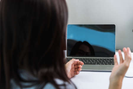 Work from home, Back of Asian young businesswoman video conference call or meeting online raise hand to explain on front laptop computer quarantines diseaseの写真素材