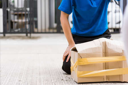 Asian young delivery man in blue uniform he emotional falling courier hold damaged cardboard box is...