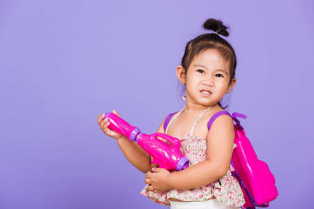 Thai child funny hold toy water pistol and smile, Happy Asian little girl holding plastic water gun, studio shot isolated on purple background, Thailand Songkran festival day national culture conceptの写真素材