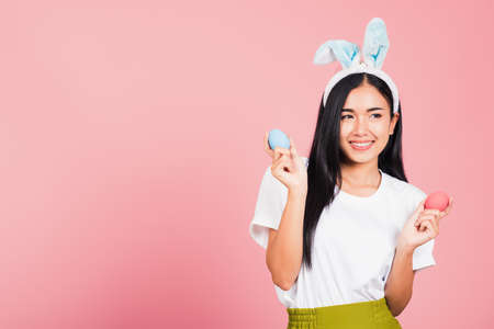 Happy Easter concept. Beautiful young woman smiling wearing rabbit ears holding colorful Easter eggs gift on hands, Portrait female looking at side away, studio shot isolated on pink backgroundの写真素材