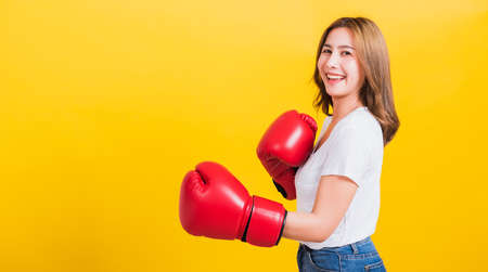 Portrait Asian Thai beautiful young woman standing smile wearing red boxing gloves she poses like a boxer, studio shot isolated on yellow background, There was copy space for textの写真素材