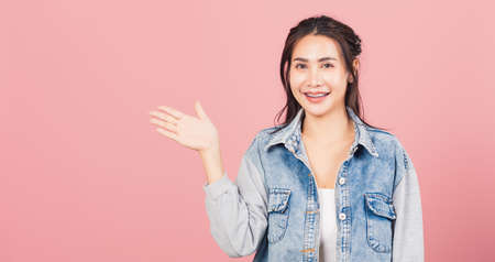 Asian happy portrait beautiful cute young woman smile standing presenting product holding something on palm away side, studio shot isolated on pink background with copy space, female show hand gestureの写真素材