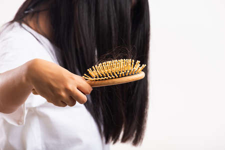 Asian woman unhappy weak hair she shows hairbrush with damaged long loss hair in the comb brush on hand, studio shot isolated on white background, medicine health care conceptの写真素材