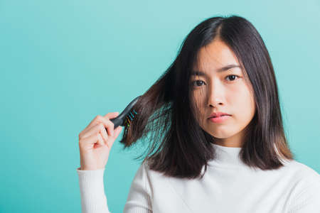 Young beautiful Asian woman upset with a comb and problem hair, Portrait female shocked suffering from hair loss problem, studio shot isolated on a blue background, medicine health conceptの写真素材