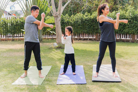 Asian young mother, father and child daughter practicing exercising stretching together before yoga...
