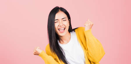 Happy Asian portrait beautiful cute young woman standing winning and surprised excited screaming open mouth raise hands, studio shot isolated pink background, Thai female wow with copy spaceの写真素材