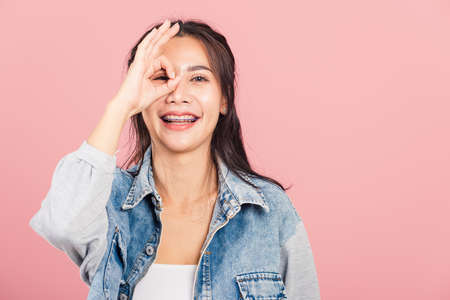 Portrait Asian beautiful young woman standing, She made finger OK symbol sign to agree near eyes...