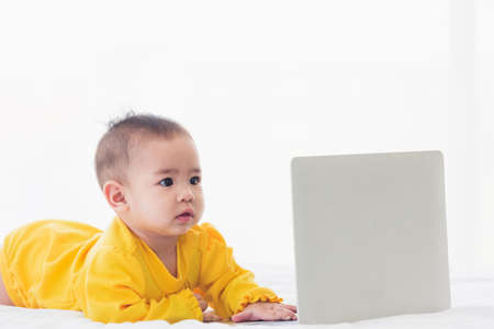 Asian little baby girl wearing a yellow dress typing hands on laptop computer keyboard and looking...