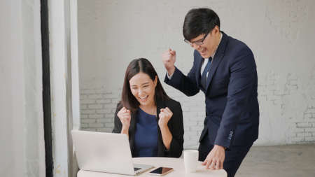Yes! Happy excited successful, Asian businessman and woman smile workstation triumphing with raised...