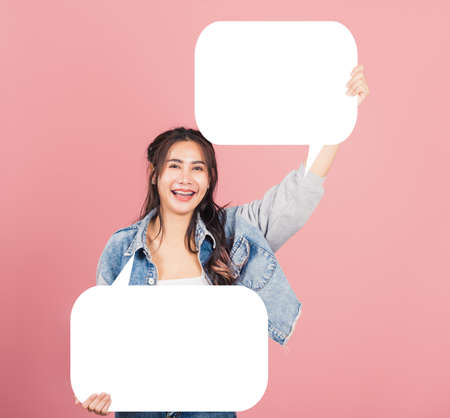 Happy Asian beautiful young woman smiling excited wear denims holding empty speech bubble sign,...