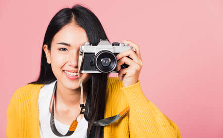 Attractive energetic happy Asian portrait beautiful young woman smiling photographer taking a picture and looking viewfinder on retro vintage photo camera ready to shoot isolated on pink backgroundの写真素材